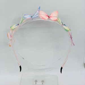 Pu&ograve; includere: Un cerchietto di plastica trasparente con cinque decorazioni di farfalle colorate. Le farfalle sono fatte di tessuto e hanno un aspetto delicato e stratificato.