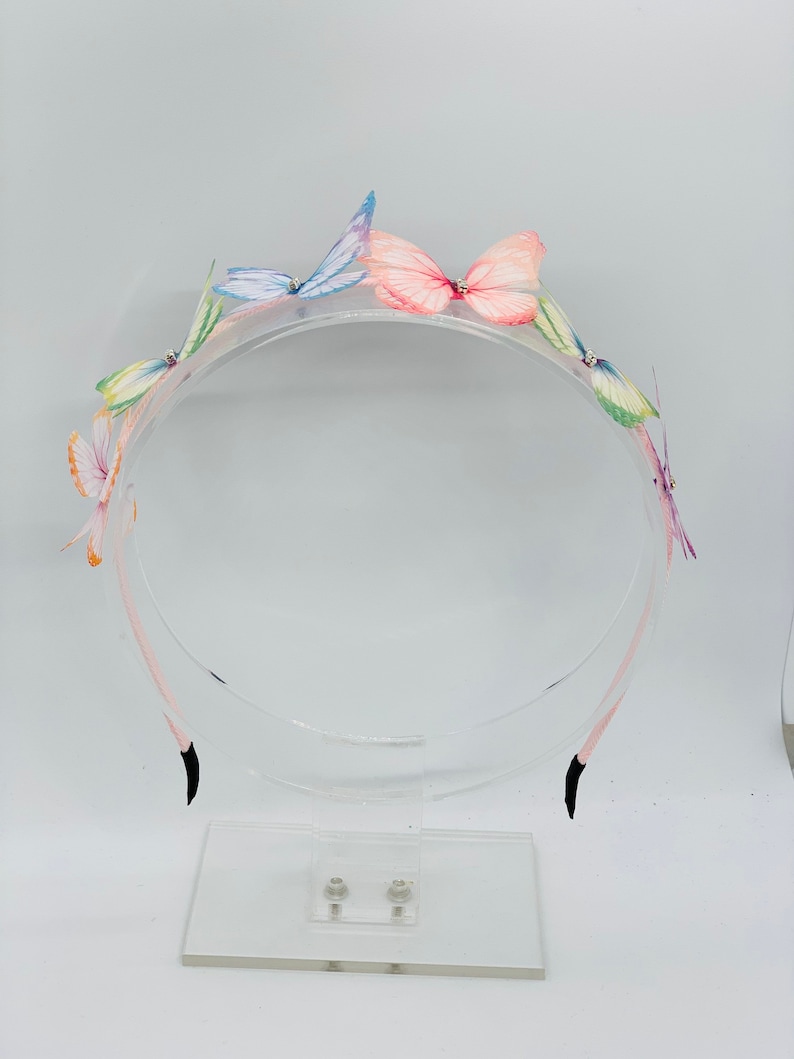 Pu&ograve; includere: Un cerchietto di plastica trasparente con cinque decorazioni di farfalle colorate. Le farfalle sono fatte di tessuto e hanno un aspetto delicato e stratificato.
