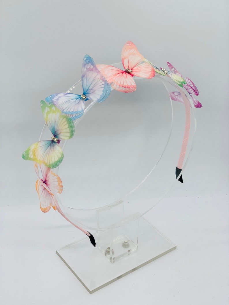 Pu&ograve; includere: Un cerchietto per capelli con una fila di farfalle colorate. Le farfalle sono fatte di tessuto trasparente e hanno ali iridescenti. Il cerchietto &egrave; rosa e ha un elastico nero.
