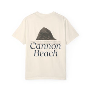 Peut inclure: Un t-shirt blanc avec un imprimé graphique d'une montagne et le texte "Cannon Beach".