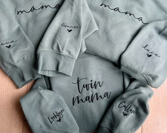 Könnte beinhalten: Drei grüne Sweatshirts mit schwarzem Sticktext. Das obere Sweatshirt sagt "mama" mit den Worten "brennen" und "ava" auf den Ärmeln. Das mittlere Sweatshirt sagt "twin mama" und das untere Sweatshirt sagt "mama" mit den Worten "Looklyn" und "Callan" auf den Ärmeln.
