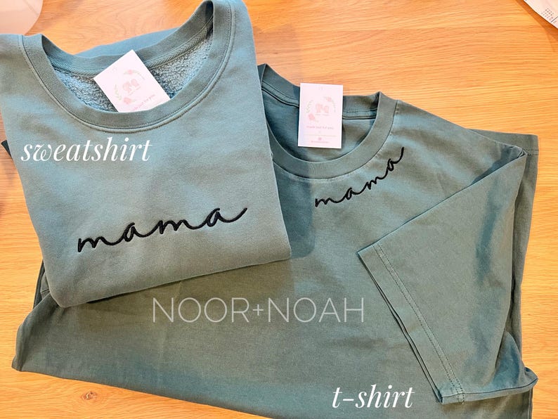 May include: A set of two green shirts with the word "mama" embroidered on them. The larger shirt is a sweatshirt and the smaller shirt is a t-shirt. The shirts are labeled "sweatshirt" and "t-shirt" in the image.