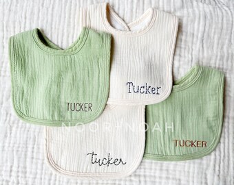 May include: Four green and white muslin baby bibs with the name "Tucker" embroidered on each one in different colors and fonts.