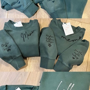 May include: A collection of green sweatshirts with various embroidered text, including "Grandma", "Nannie", "Mama", "Haylee Holden Hallie", "Memo", "Paddle Colt Riley", "Lolli", and "Auntie".