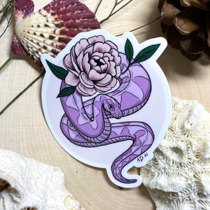 May include: A purple snake coiled around a pink flower with green leaves. The snake and flower are on a white background with a pink circle around them. The sticker has the text "AD 21" in the bottom right corner.
