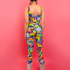 May include: A woman wearing a blue, green, yellow, and pink jumpsuit with a psychedelic mushroom print. The jumpsuit has a scoop neck and sleeveless design. She is wearing silver fringe boots.