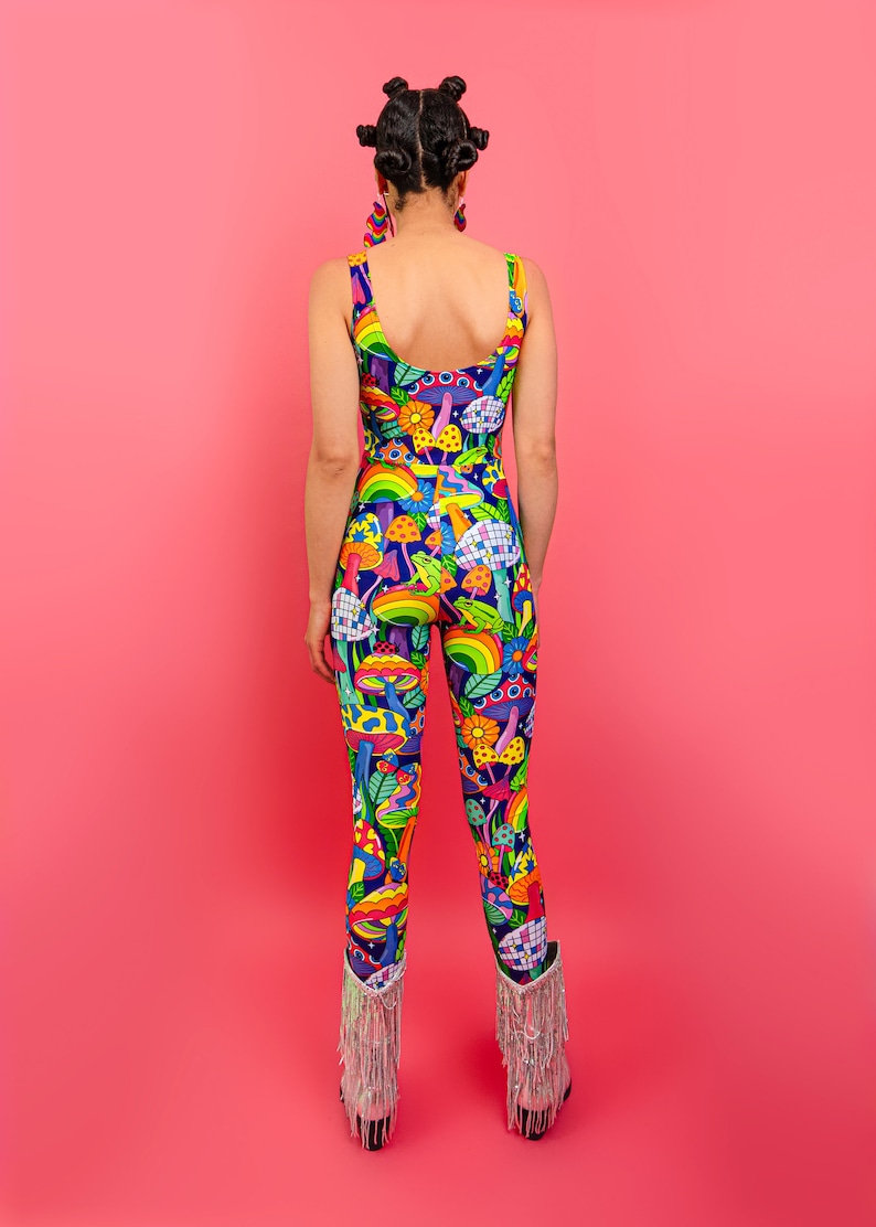 May include: A woman wearing a blue, green, yellow, and pink jumpsuit with a psychedelic mushroom print. The jumpsuit has a scoop neck and sleeveless design. She is wearing silver fringe boots.