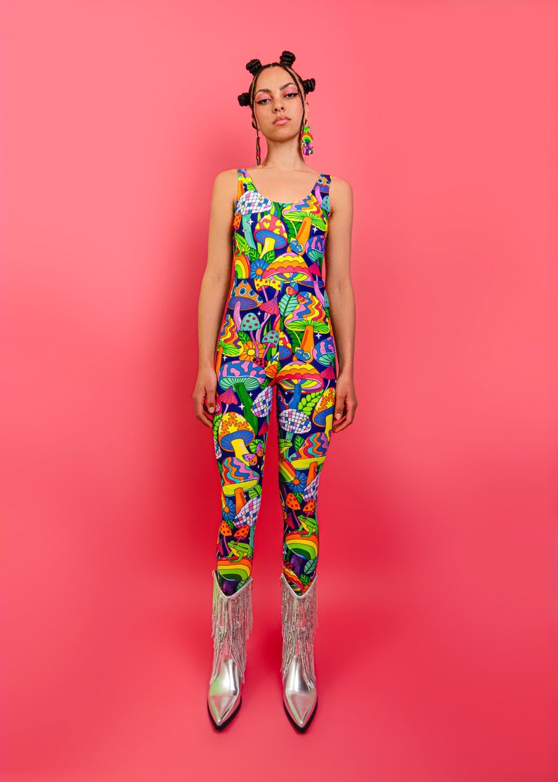 May include: A person wearing a blue and multi-colored jumpsuit with a psychedelic mushroom print. The jumpsuit has a scoop neck and sleeveless design. The person is wearing silver cowboy boots with fringe.