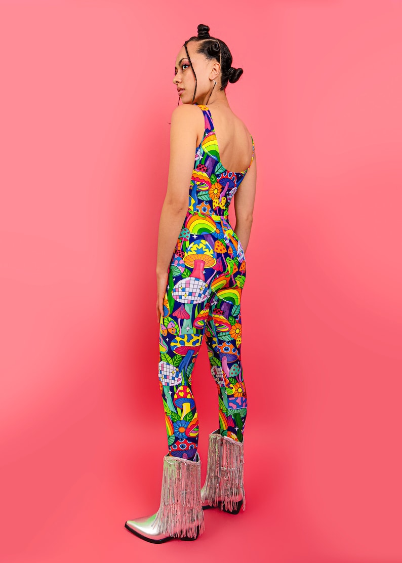 May include: A person wearing a colorful jumpsuit with a psychedelic mushroom and rainbow pattern. The jumpsuit has a scoop neck and thin straps. The person is wearing silver cowboy boots with fringe.