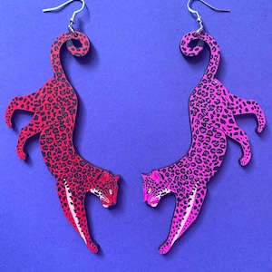 Op de afbeelding: Een paar oorhangers met een roze en zwart luipaardprint ontwerp. De oorbellen zijn gemaakt van hout en hebben zilveren haakjes.