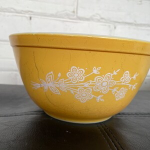 May include: A yellow mixing bowl with a white floral design. The bowl has a vintage look and is made of ceramic.