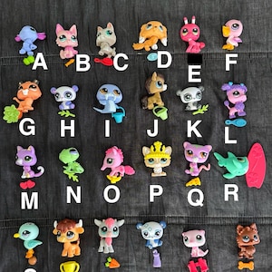 Puede incluir: Una colección de 26 mascotas de plástico de colores, cada una con una etiqueta de letra de la A a la X. Las mascotas están dispuestas en cuatro filas, con seis a siete mascotas en cada fila. Las mascotas incluyen una variedad de animales, como gatos, perros, pájaros, peces y un panda.