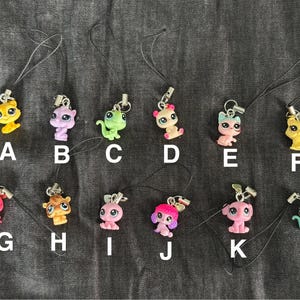 May include: A set of 12 colorful animal charms with black string attached. The charms are in the shape of a cat, dog, lizard, and other animals. The charms are perfect for adding a touch of personality to your keys, bags, or other accessories.