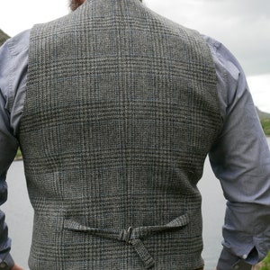May include: A gray and blue plaid vest with an adjustable back strap. The vest is made of a tweed fabric and has a classic design.