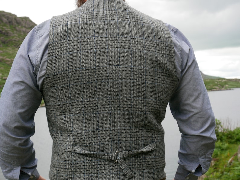 May include: A gray and blue plaid vest with an adjustable back strap. The vest is made of a tweed fabric and has a classic design.