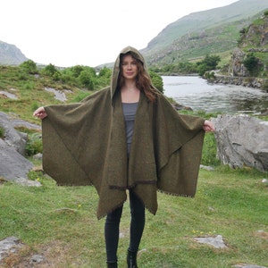 May include: A green hooded cloak with a fringed edge. The cloak is made of a soft, textured fabric and is worn by a person standing in a natural setting.
