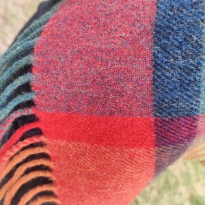 May include: A red, blue, and orange plaid scarf with fringe. The scarf is made of a soft, fuzzy material.