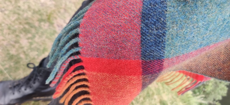 May include: A red, blue, and orange plaid scarf with fringe. The scarf is made of a soft, fuzzy material.