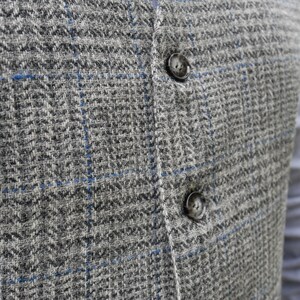 May include: A close-up of a gray and blue plaid vest with two black buttons. The vest is made of a soft, textured fabric.