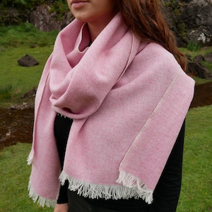 May include: A pink wool scarf with a white fringe. The scarf is folded and draped around a person's neck.