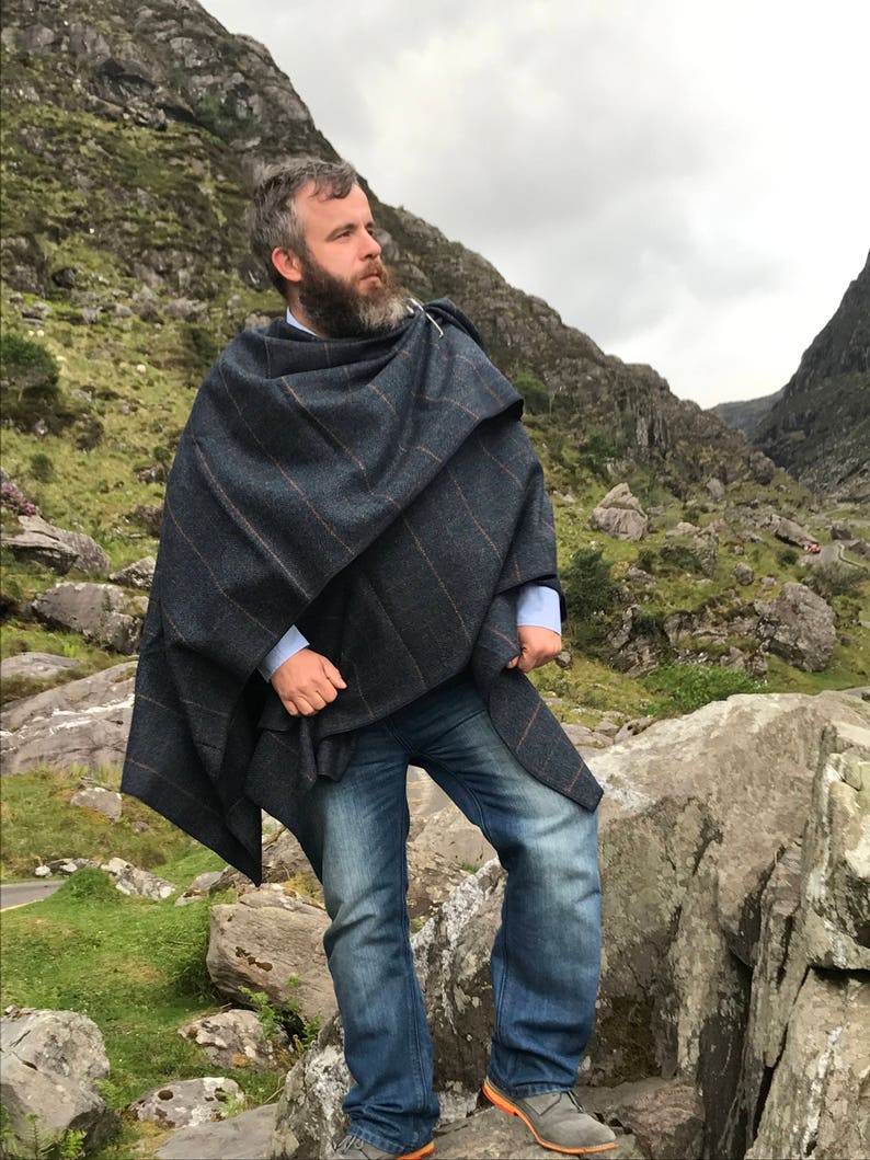 May include: A person wearing a blue and brown striped wool shawl with a fringe. The shawl is draped over the person's shoulders and is worn with blue jeans.