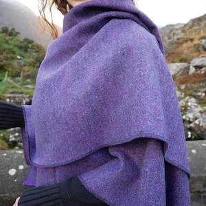 May include: A purple tweed shawl with a layered design. The shawl is a vibrant shade of purple with flecks of other colors. The fabric appears to be thick and warm, suitable for cooler weather. The shawl is draped over the shoulders.