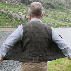 Peut inclure: Un gilet en tweed &agrave; carreaux vert, marron et rouge avec une fermeture &agrave; boucle dans le dos. Le gilet est d&eacute;boutonn&eacute; et la personne qui le porte est dos &agrave; la cam&eacute;ra.