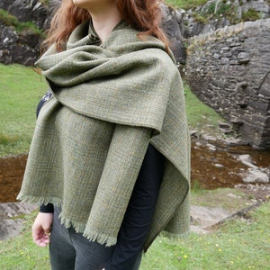 Peut inclure: Une écharpe en tweed vert et marron avec une bordure frangée. L'écharpe est drapé sur les épaules d'une personne et est portée à l'extérieur.