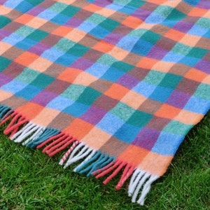 Puede incluir: Una manta de picnic a cuadros de colores con un borde con flecos. La manta está hecha de una tela suave y tejida, ideal para reuniones al aire libre.