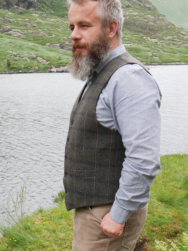 Peut inclure: Un homme portant un gilet &agrave; carreaux vert et rouge sur une chemise boutonn&eacute;e bleu clair. Il a une longue barbe grise et se tient devant un lac.