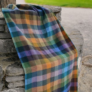 Könnte beinhalten: Eine bunte karierte Wolldecke mit Fransen, die über eine Steinmauer gelegt ist. Die Decke hat Farbtöne in Blau, Grün, Orange und Braun.