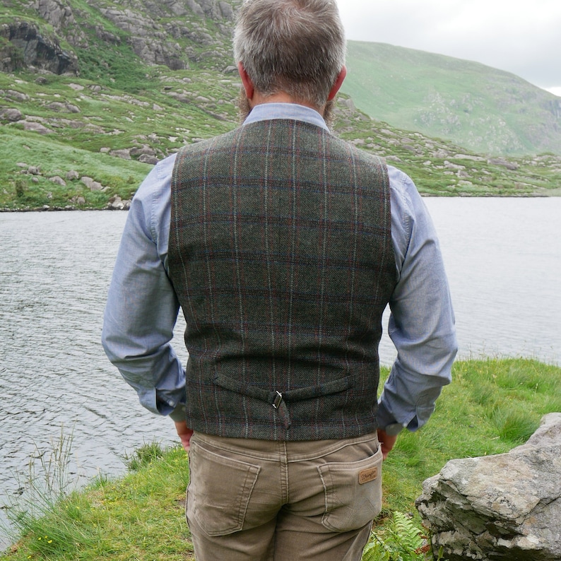 Peut inclure: Un gilet en tweed &agrave; carreaux vert, marron et rouge avec une sangle en cuir marron dans le dos. Le gilet est de style classique.