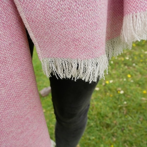 May include: A pink and white woven shawl with a fringe border. The shawl is draped over a person's shoulders.