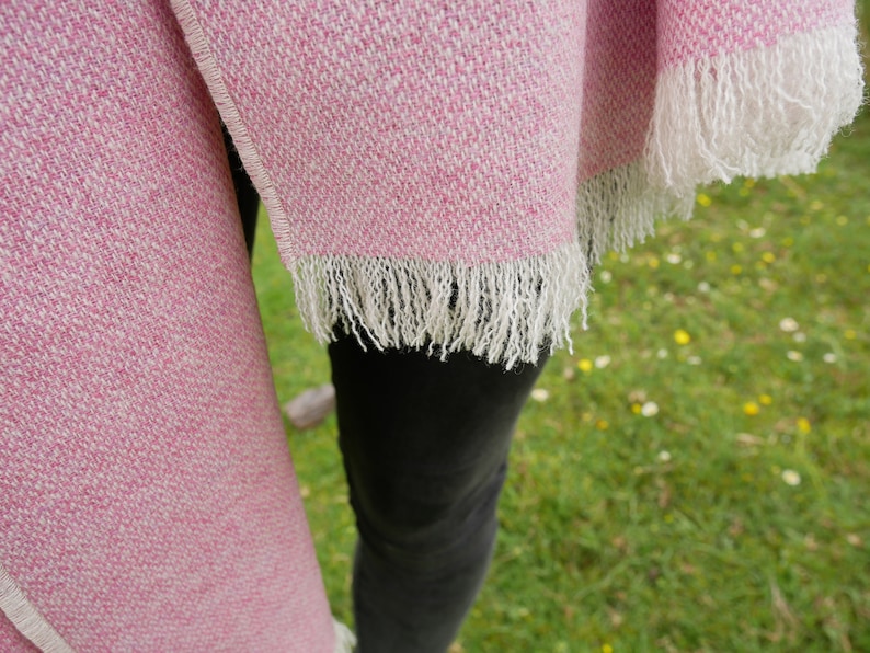 May include: A pink and white woven shawl with a fringe border. The shawl is draped over a person's shoulders.