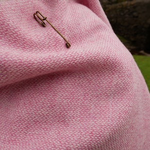 May include: A pink and white woven throw blanket with a gold safety pin.