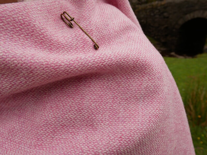 May include: A pink and white woven throw blanket with a gold safety pin.