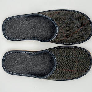 Pode incluir: Um par de chinelos de biqueira aberta com interior cinza escuro e exterior em tweed espinha de peixe em tons de verde, castanho e vermelho. Os chinelos têm uma borda azul escuro e costuras brancas.