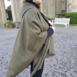 May include: A green and gold hooded shawl with a fringed edge. The shawl is draped over a person's shoulders and is worn with black pants.