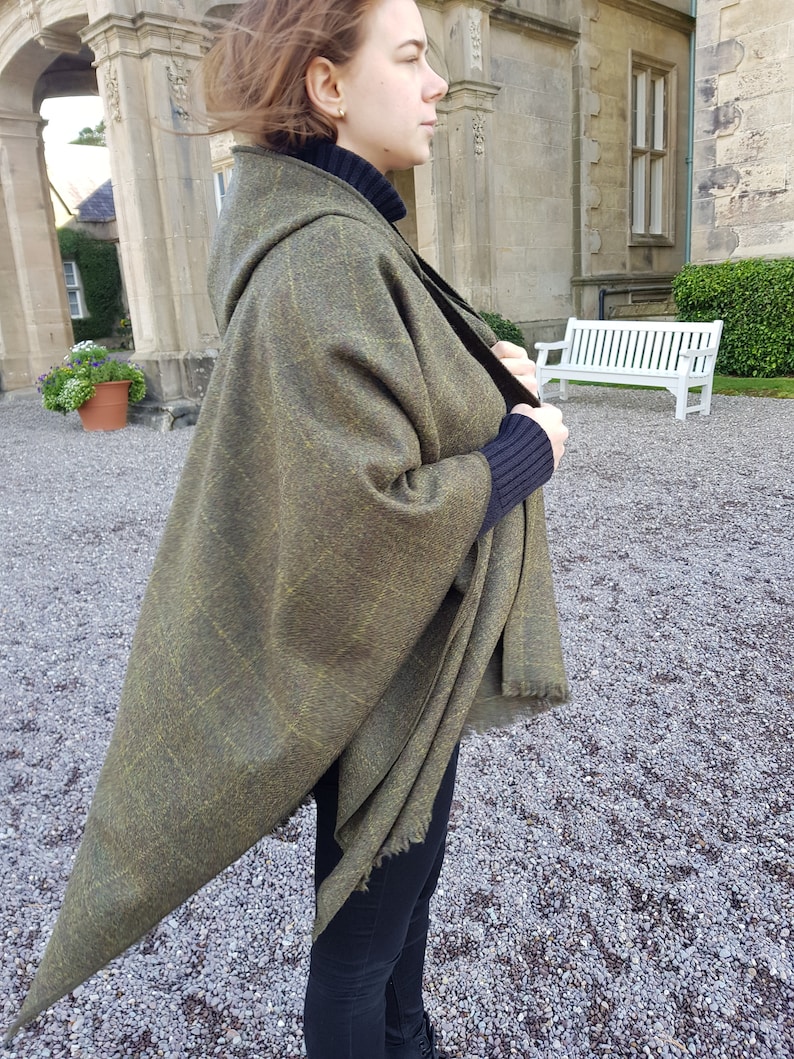 May include: A green and gold hooded shawl with a fringed edge. The shawl is draped over a person's shoulders and is worn with black pants.