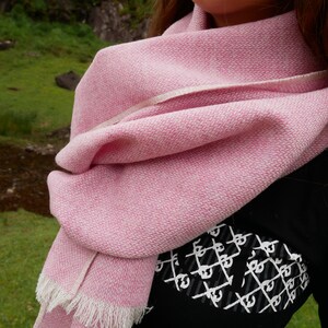 May include: A pink and white woven scarf with a fringed edge. The scarf is folded and draped around a person's neck.