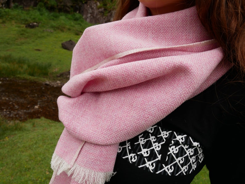 May include: A pink and white woven scarf with a fringed edge. The scarf is folded and draped around a person's neck.