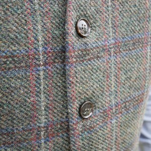 Peut inclure: Gros plan sur un gilet en tweed avec deux boutons marrons. Le gilet est &agrave; carreaux dans des tons de vert, marron, rouge et bleu.