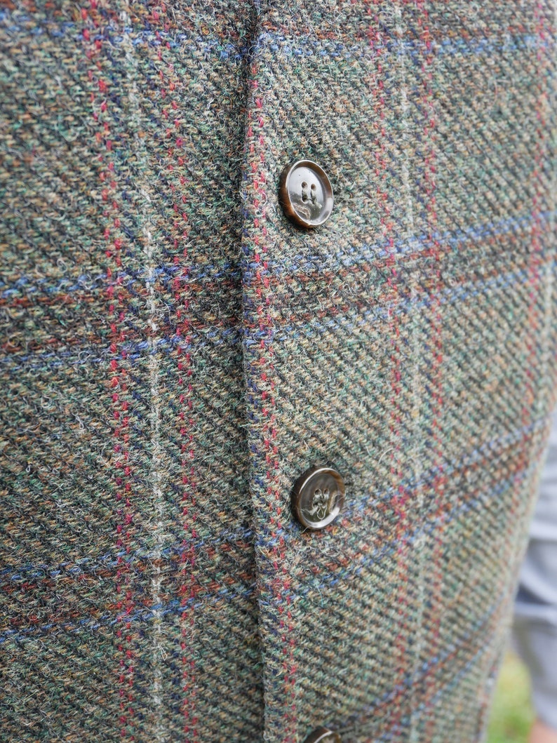Peut inclure: Gros plan sur un gilet en tweed avec deux boutons marrons. Le gilet est &agrave; carreaux dans des tons de vert, marron, rouge et bleu.