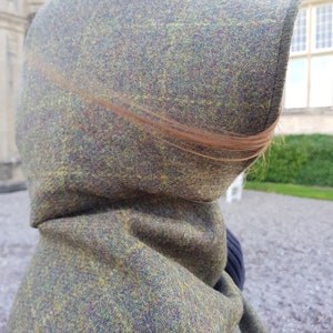 May include: A hooded cloak made of a green, brown, and yellow tweed fabric. The hood is pulled up and the fabric is textured.