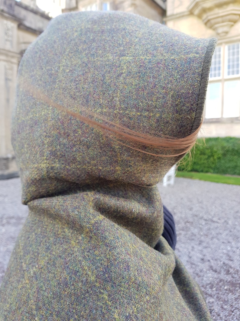 May include: A hooded cloak made of a green, brown, and yellow tweed fabric. The hood is pulled up and the fabric is textured.