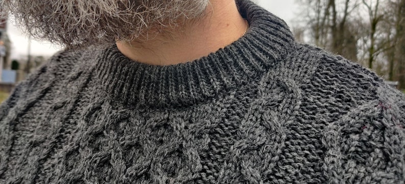 May include: A close-up of a gray cable knit sweater with a ribbed collar.
