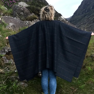 May include: A dark blue plaid poncho with a fringed edge. The poncho is worn by a person standing in a mountainous landscape.
