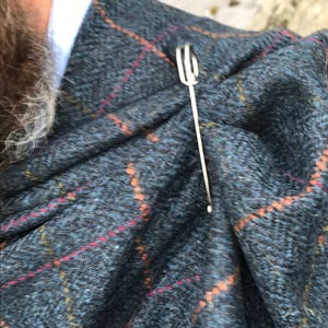 May include: A silver scarf pin with a looped design, holding a plaid scarf in place.