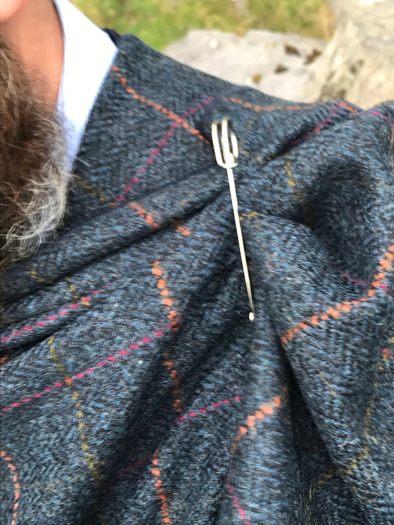 May include: A silver scarf pin with a looped design, holding a plaid scarf in place.