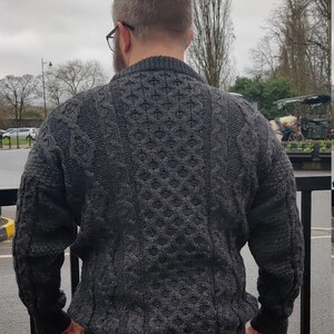 May include: A dark gray cable knit sweater with a textured pattern. The sweater has a high neckline and long sleeves.